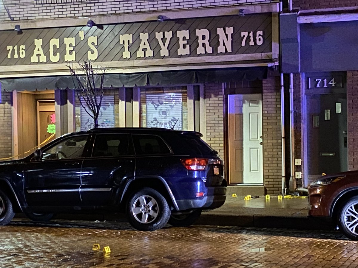 Evidence markers are on the street and sidewalk in front of Aces Tavern. A gun next to one of the markers. Police said a 21-year-old man is detained. and it appears the victim and the 21-year-old man shot at each other.